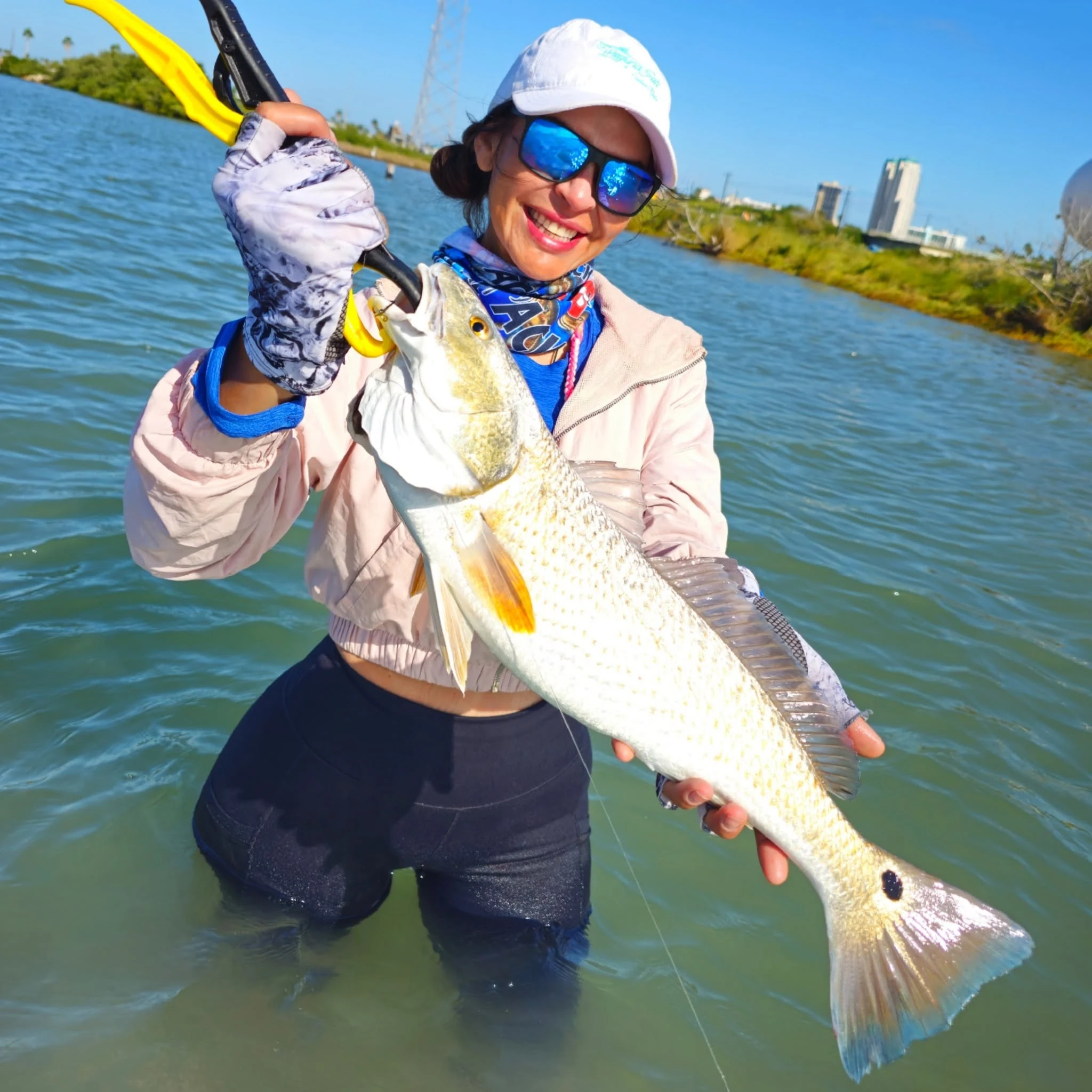 Captain Eva smiling and holding a redfish while standing in the water